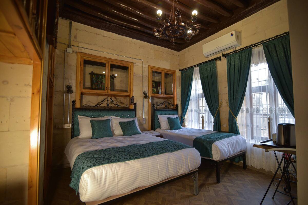 A room with two beds, wooden headboards, a chandelier, and a television on a desk.