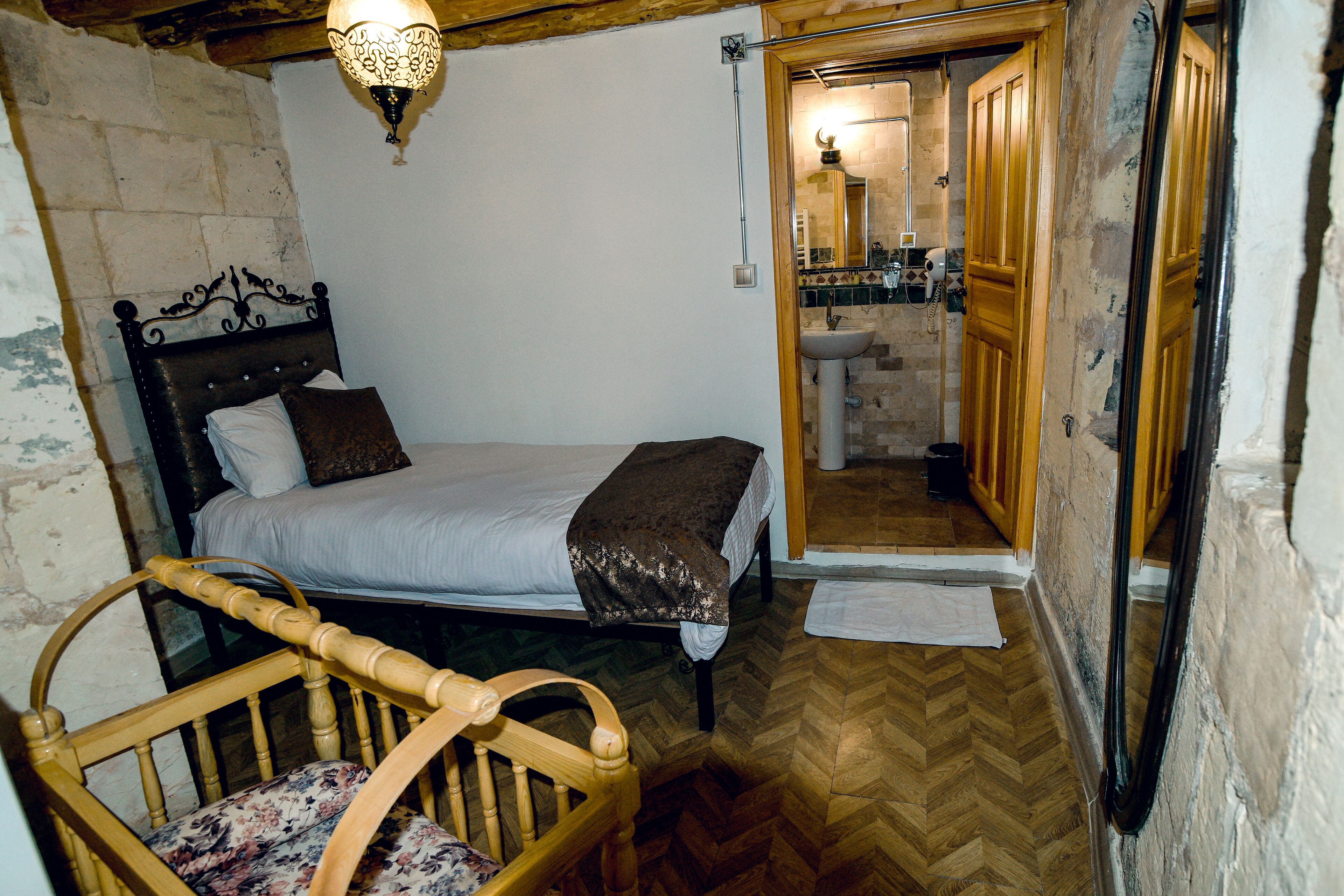 Un dormitorio con cama, una silla de madera y un baño visible a través de una puerta abierta.