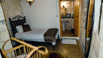 Un dormitorio con cama, una silla de madera y un baño visible a través de una puerta abierta.