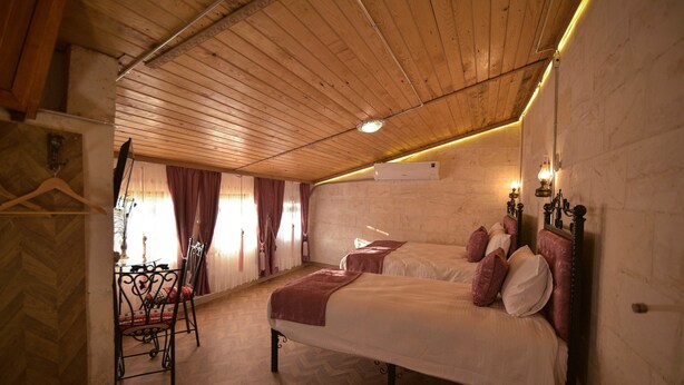 Una habitación con dos camas, techo de madera, una mesa con sillas y una ventana con cortinas.