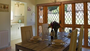 Un coin repas avec une table en bois dressée pour deux personnes, un lustre et une vue dégagée sur l’extérieur grâce à de grandes fenêtres.