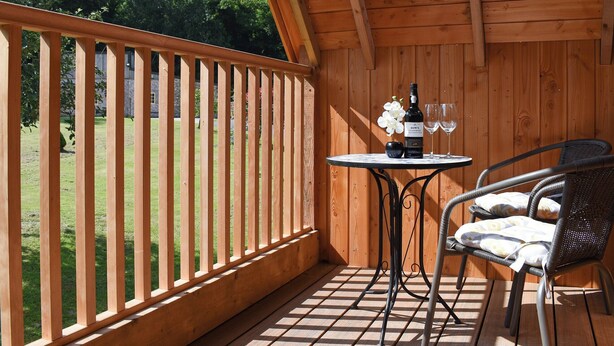 Une terrasse en bois avec une table et des chaises, une bouteille de vin et un vase de fleurs.