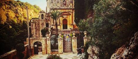 A historic church with a bell tower, surrounded by lush greenery and rocky terrain.