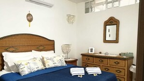 Ein Schlafzimmer mit einem hölzernen Kopfteil, einem Bett mit blauer Bettwäsche, dekorativen Kissen, einem Nachttisch mit Lampe, einer Kommode und einem Spiegel an der Wand.