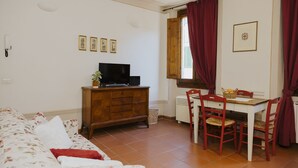 Una habitación con cama, cómoda de madera, televisor, mesa de comedor con sillas y ventana con cortinas.