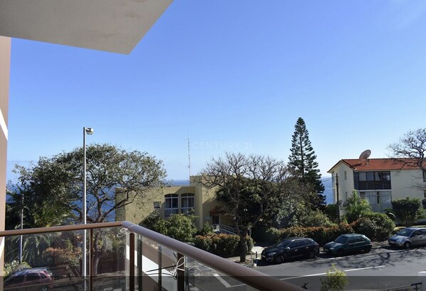 Un quartier résidentiel offrant une vue dégagée sur un immeuble doté d’une antenne parabolique, des voitures garées et des arbres.