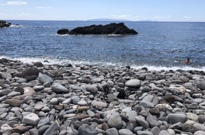 Une plage rocheuse, parsemée de gros galets, d’où l’on a une vue dégagée sur l’océan.