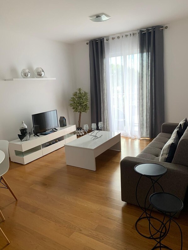 A modern living room with a flat-screen TV on a white console, a grey sofa, and a coffee table.