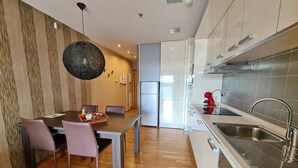 Una cocina moderna con armarios blancos, un lavamanos de acero inoxidable y una mesa de comedor de madera con sillas.