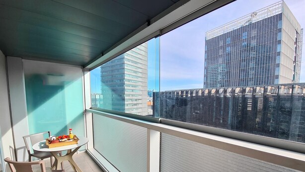Un balcón con mesa y sillas, vista de edificios modernos y una puerta de vidrio.