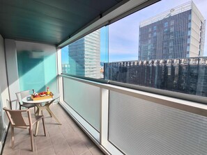 Un balcón con mesa y sillas, vista de edificios modernos y una puerta de vidrio.
