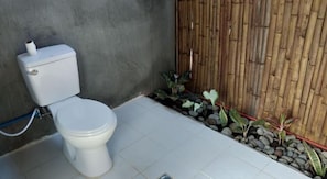 A toilet with a bamboo wall and a small garden area with rocks and plants.