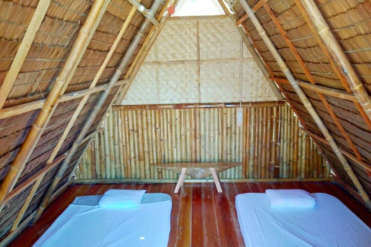 Una habitación pequeña y triangular con dos camas y un banco. El techo y las paredes son de bambú.