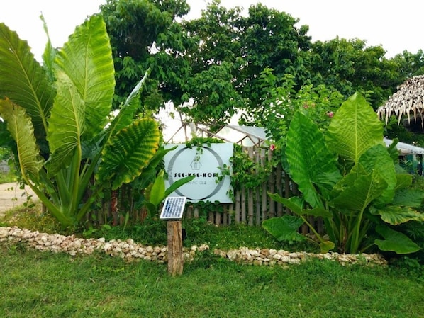 A garden area with large green leaves, a wooden fence, and a sign with a logo.