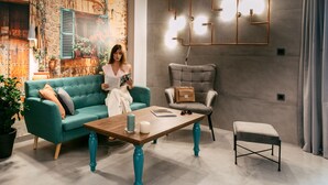 A cozy living room with a teal sofa, a wooden coffee table, and a grey armchair. There is a wall-mounted light fixture above the armchair. - Views, Pool, Garden, BBQ, Playground, Tennis Table (CHANIA)