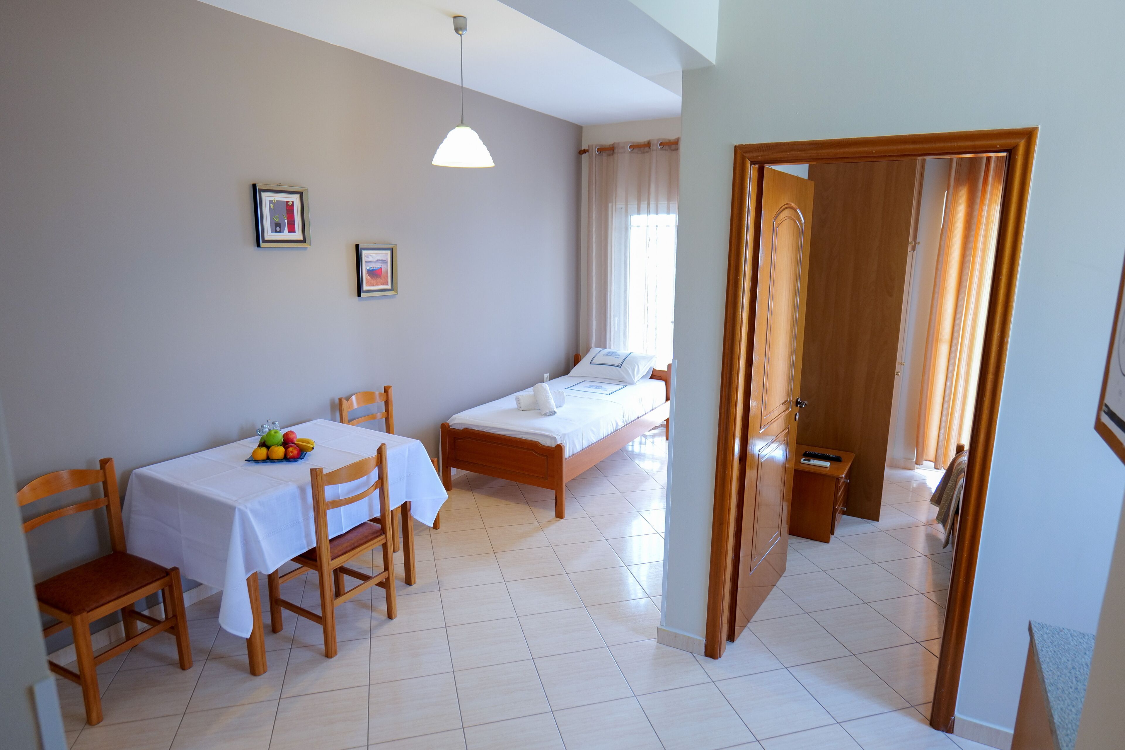 A bedroom with a bed, a bedside table, a chair, and a small table with fruit.