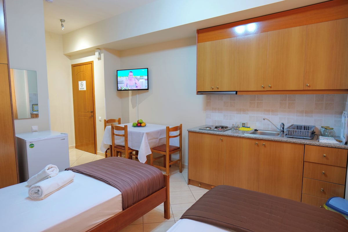 Une chambre d’hôtel avec deux lits, une petite kitchenette, une table à manger avec des chaises et un téléviseur fixé au mur.