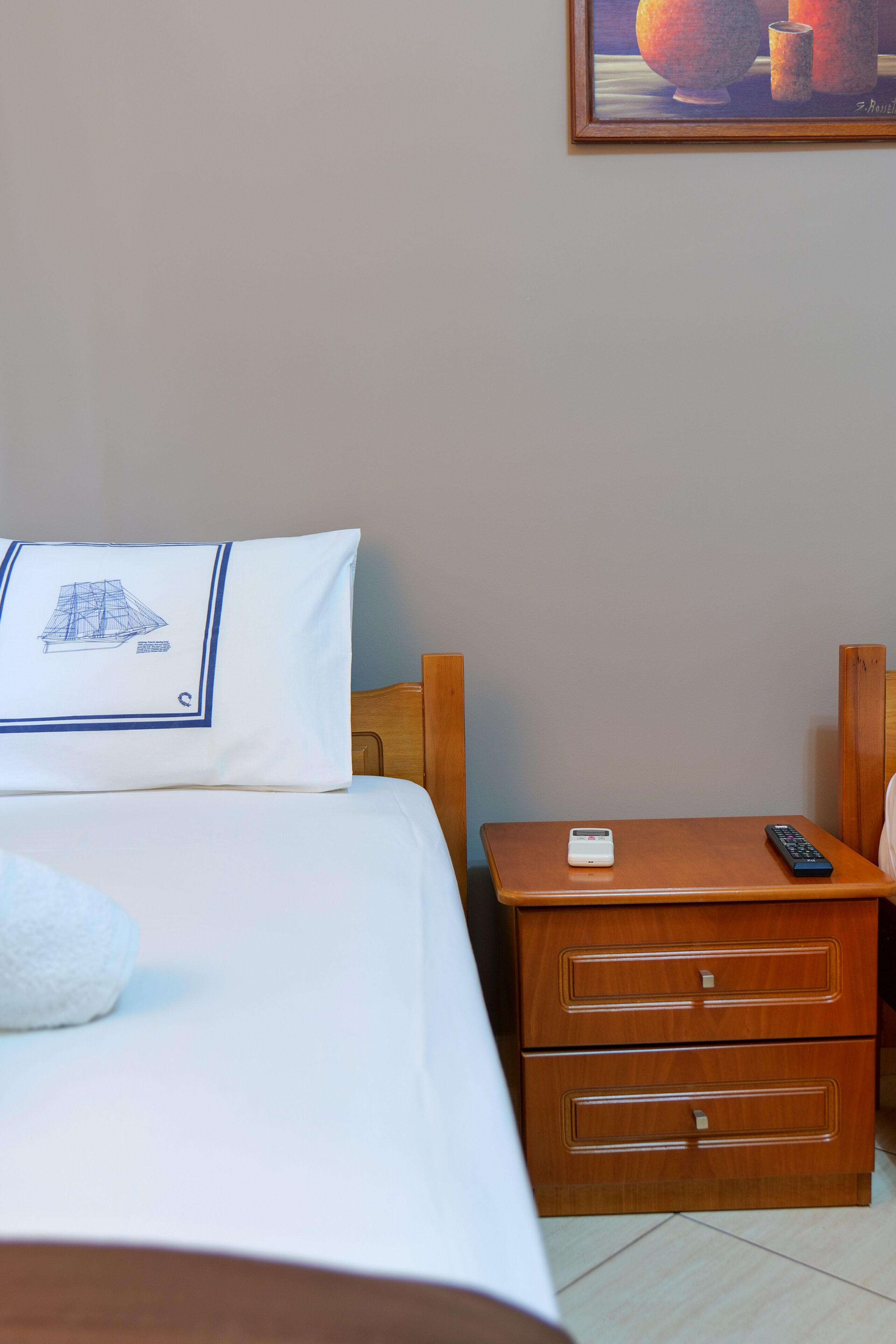 A hotel room with a bed, a nightstand with a remote control, and a small table.