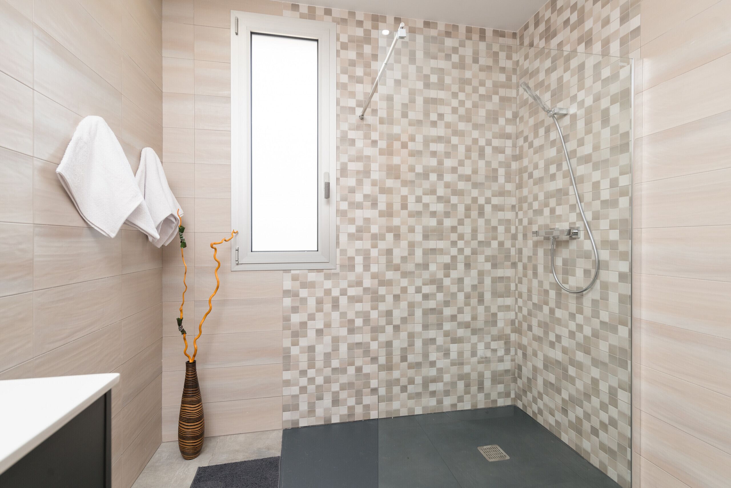 Ein modernes Badezimmer mit Dusche, gefliesten Wänden und einem Fenster.