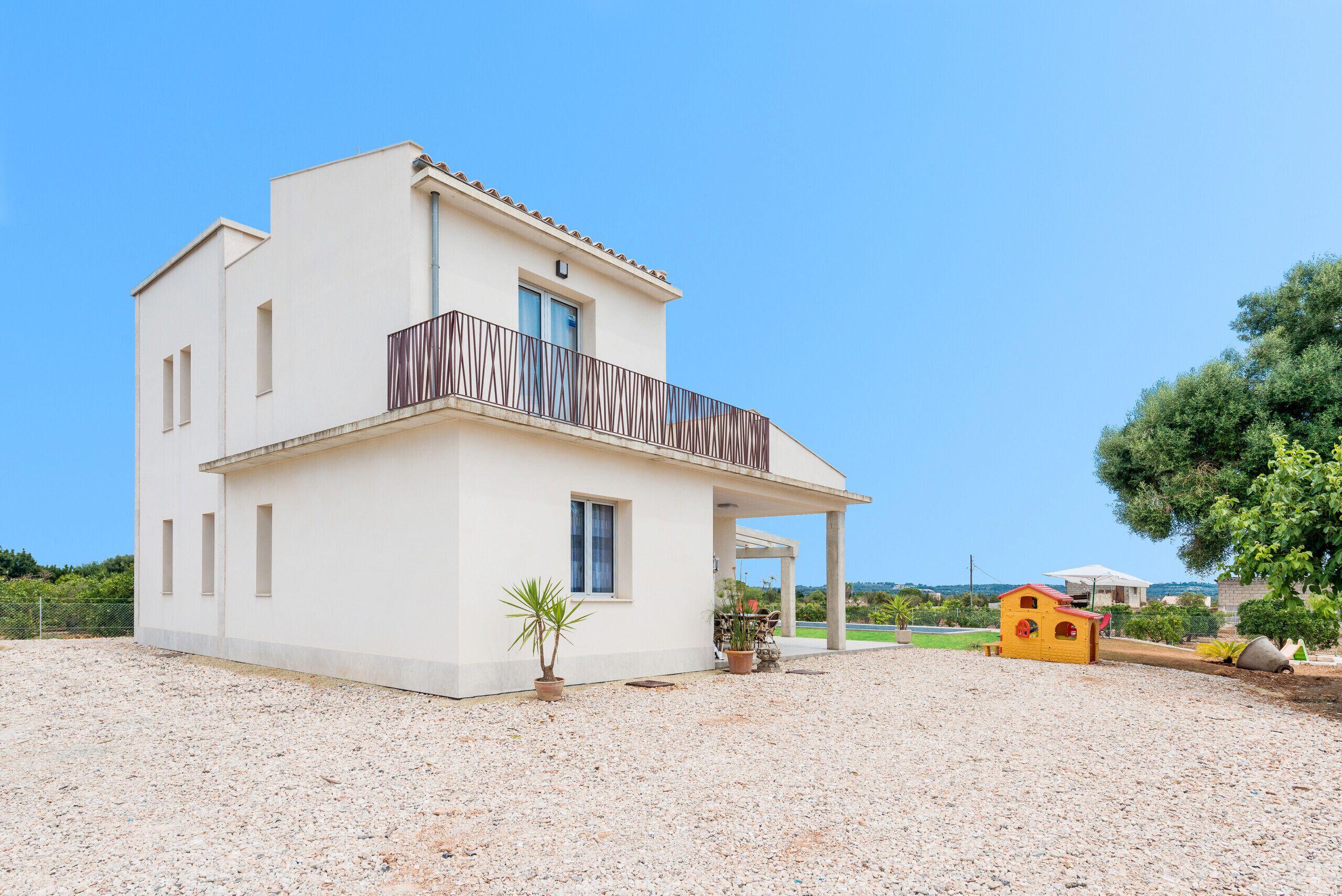 A two-story house with a balcony, a small garden, and a yellow playhouse.