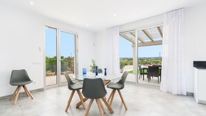 A modern dining area with a glass table and chairs, a view of the outdoors, and a sliding glass door leading to a patio. - Very modern villa with private pool and huge garden in the heart of Mallorca. (Llubi)