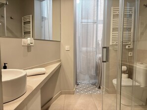 A bathroom with a glass shower enclosure, a white sink, and a toilet. - Chic studio in a perfect location in Barcelona (Barcelona)