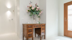 Een houten bureau met lades en een bloevas, geplaatst in een hoek met een deur en lichtschakelaar op de muur.