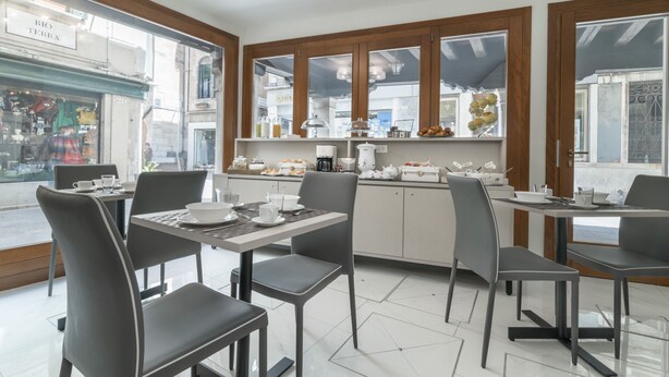 Een eethoek met tafels en stoelen, een keuken met kasten en apparatuur, en grote ramen met uitzicht op de straat.