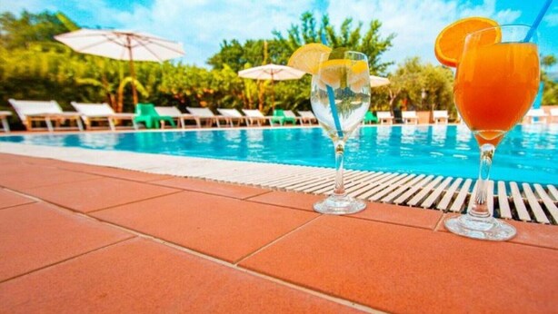 A poolside area with lounge chairs and umbrellas, and two glasses of orange beverage on the poolside. - Residence Medimare ~ TWO-ROOM APARTMENT 14 (Patti Sicilia)