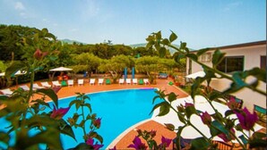 A swimming pool with lounge chairs and umbrellas, surrounded by greenery and a building in the background. - Residence Medimare ~ TWO-ROOM APARTMENT 14 (Patti Sicilia)
