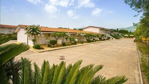 A row of single-story buildings with a tiled roof, surrounded by greenery and a clear sky. - Residence Medimare ~ TWO-ROOM APARTMENT 14 (Patti Sicilia)