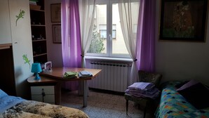 A bedroom with a bed, a desk, a chair, a radiator, and a window with curtains. - Apartment with 2 bedrooms and kitchen (Avezzano)