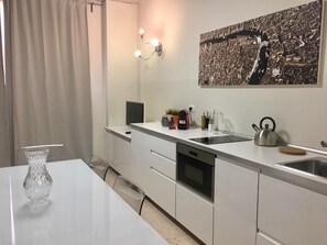 Une cuisine moderne avec un plan de travail blanc, une bouilloire, une machine à café et une grande fenêtre.