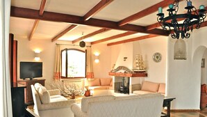 A living room with a piano, sofas, a television, and a chandelier.