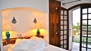 A bedroom with a bed, two wall-mounted lamps, a wooden door, and a view of the outdoors.