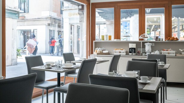 Una cafetería moderna con ventanas amplias, una estación de café y asientos para los clientes.
