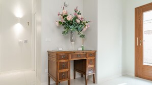 Un escritorio de madera con cajones, un florero con flores y una puerta en un pasillo luminoso.