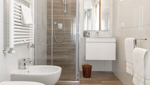 Un baño moderno con ducha envuelta en vidrio, un lavamanos blanco y un inodoro.