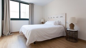 A neatly arranged bedroom with a large bed, two bedside lamps, a decorative wall piece, and a wicker side table. - Albareda 6 - Two Bedroom Apartment, Sleeps 4 (Sevilla)