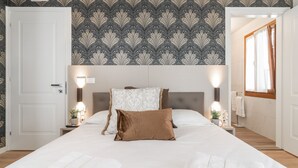 A hotel room with a patterned wallpaper, a bed with white and brown bedding, two bedside tables with lamps, and a window with curtains. - Room 3 - Grifoni Boutique Hotel (Venice)