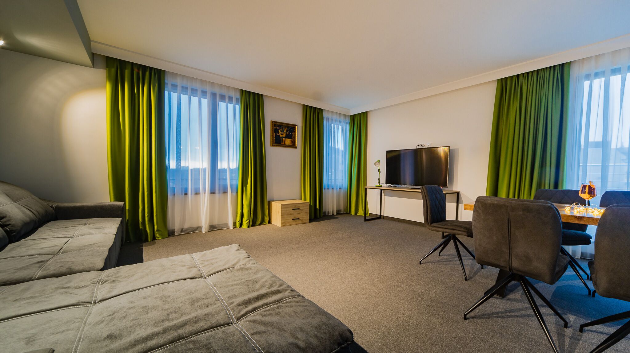 A modern hotel room with a sofa, a desk with a TV, and green curtains.