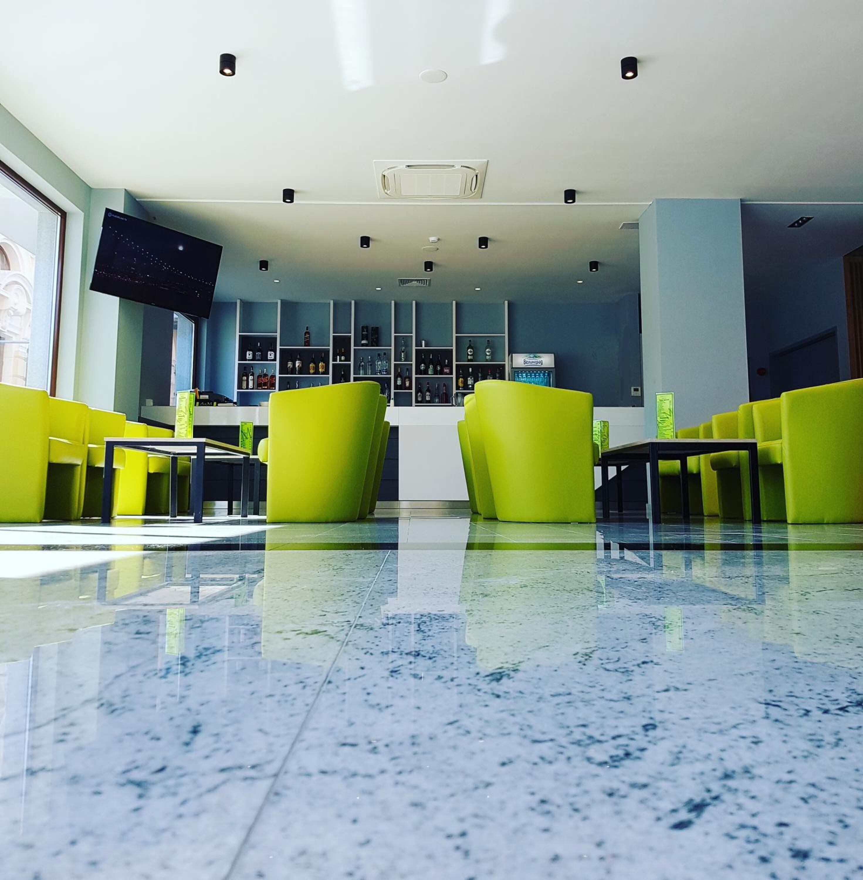 Un vestíbulo moderno con asientos de color amarillo brillante, un televisor de pantalla plana grande y una zona de bar con estantes llenos de botellas.