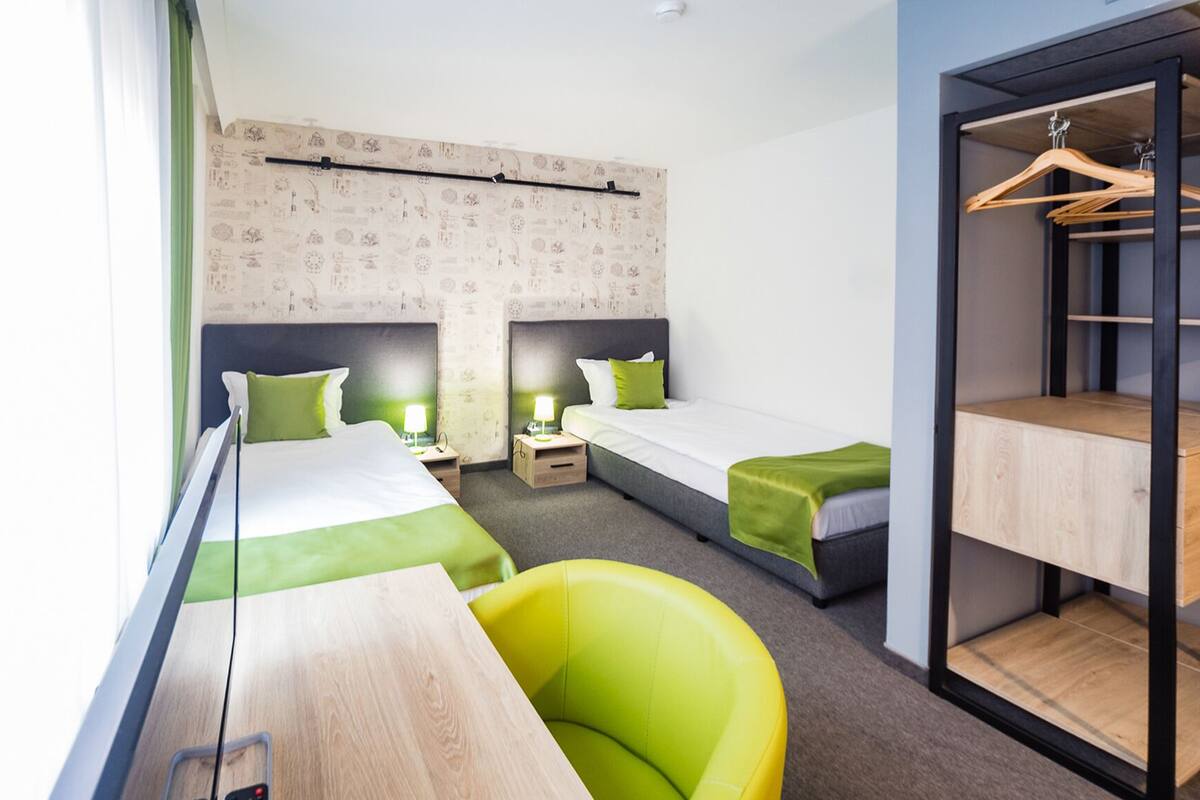 Une chambre d’hôtel avec deux lits simples, un bureau, une chaise et une armoire.
