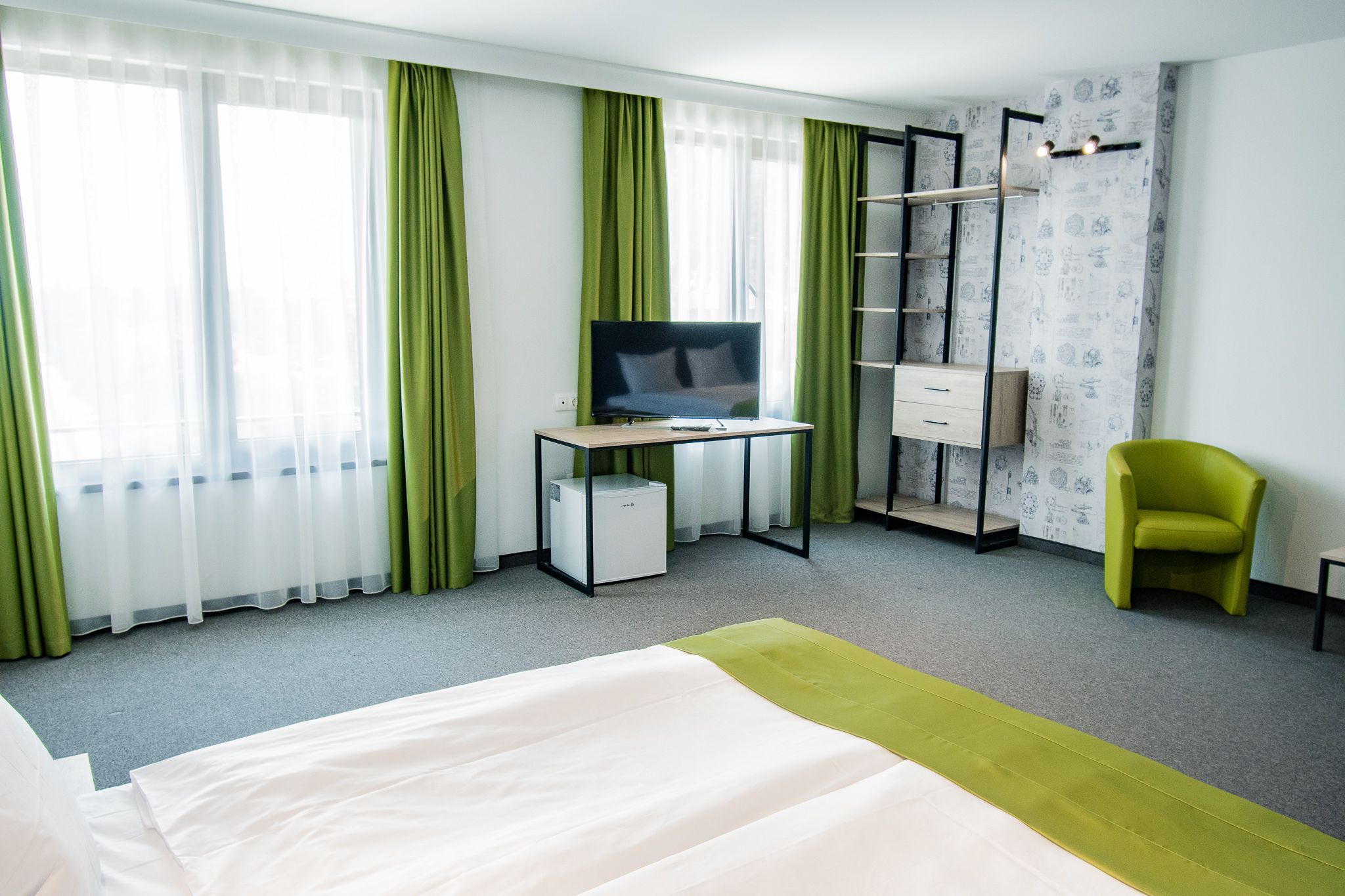 Une chambre d’hôtel comprenant un lit, un bureau avec une télévision, un petit espace de rangement, une chaise et une armoire avec une échelle.