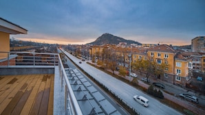 A cityscape with a prominent hill in the background, a clear sky, and a road with vehicles. - A&M Hotel - Plovdiv (Plovdiv)