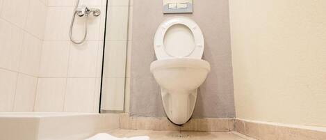 A bathroom with a toilet, a shower, and a towel on the floor.