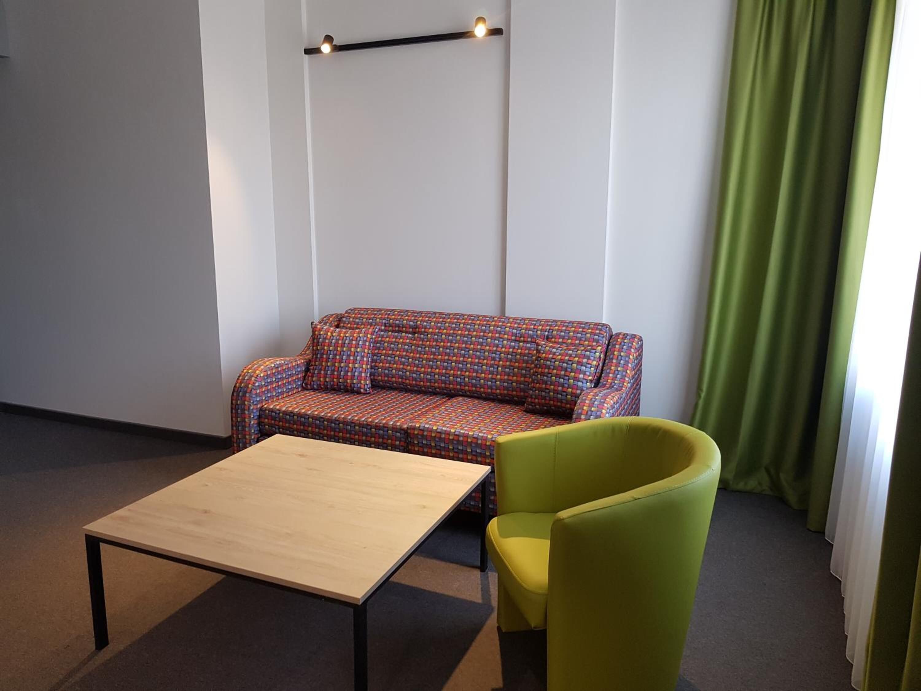Una habitación con un sofá estampado, un sillón verde y una mesa de madera.