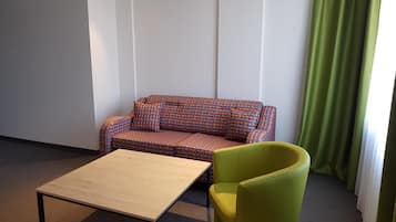 Una habitación con un sofá estampado, un sillón verde y una mesa de madera.
