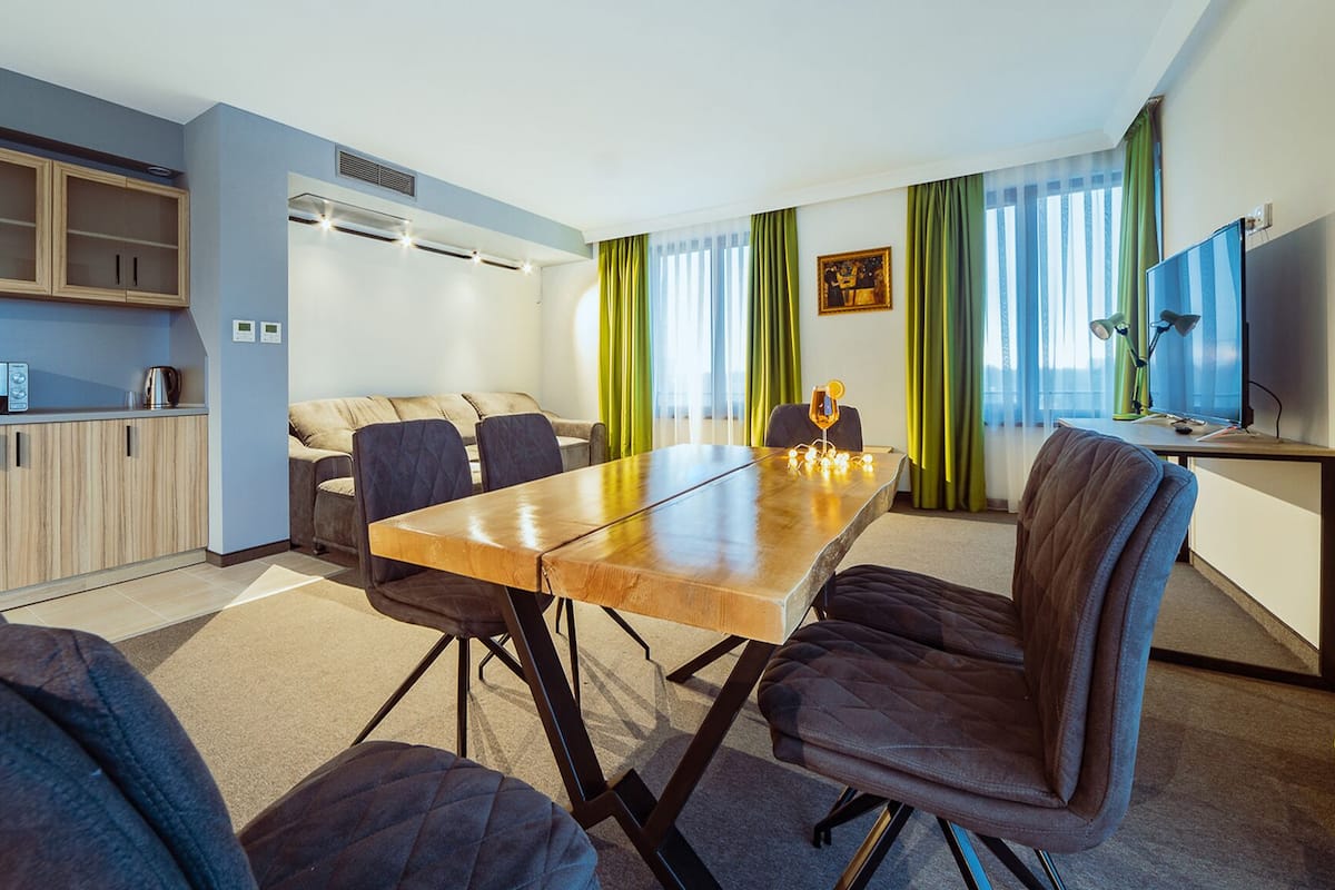 Une chambre d’hôtel moderne dotée d’un coin repas, d’une kitchenette et d’une grande fenêtre avec des rideaux.