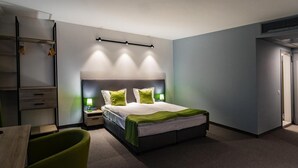 A modern hotel room with a large bed, bedside tables with lamps, a green chair, and a wardrobe. - A&M Hotel - Plovdiv (Plovdiv)